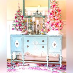 a blue dresser with pink christmas trees on top and other decorations in the back ground