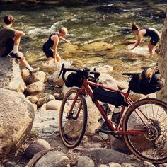 a bike parked next to a river with people on the rocks in the water behind it