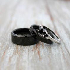 two wedding rings with black and white diamonds are on a wooden surface, one is in the shape of a skull