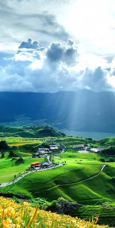 the sun shines through clouds over green hills and fields with yellow flowers on them