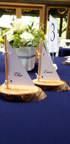 two small sailboats are sitting on a table with blue linens and white flowers