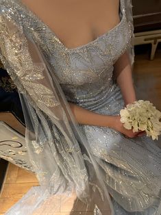 a woman in a wedding dress sitting on the floor holding a bouquet of white flowers