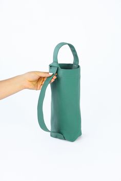 a hand is holding a green bag on a white background with the handle extended up