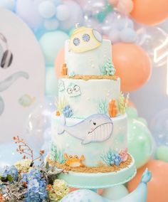 there is a three layer cake with an ocean theme on it and balloons in the background