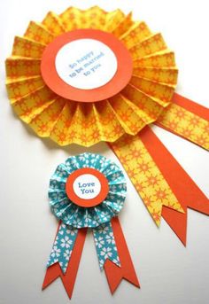 two award ribbons with the words love you written on one side and an orange rosette in the middle