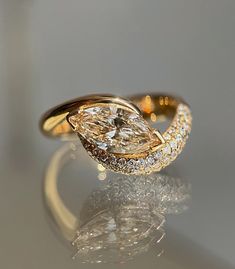 a yellow gold ring with a pear shaped diamond on it's side, sitting on a reflective surface