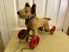 a small dog riding on top of a wooden toy car with wheels and red spokes