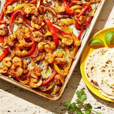 a pan filled with shrimp, peppers and tortillas next to a yellow plate