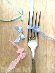 a fork with blue ribbon on it sitting next to a pink and white bow tie