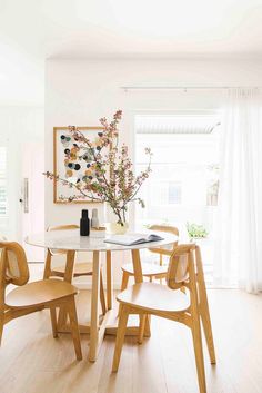 a dining room table with chairs and a vase filled with flowers on top of it