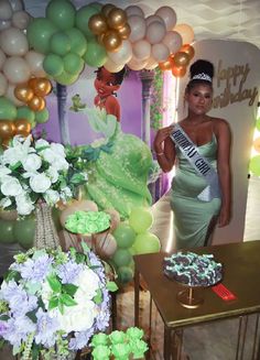 a woman in a green dress standing next to a table with cake and flowers on it