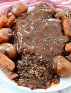 a white plate topped with meat covered in gravy and carrots on top of a table