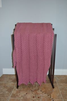 a crocheted blanket is draped on a wooden stand in a room with tile flooring