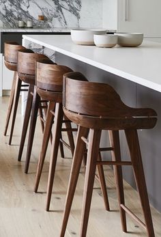 four wooden stools sitting on top of a white counter next to a kitchen island