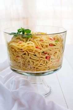 a glass bowl filled with pasta and vegetables on top of a white cloth covered table