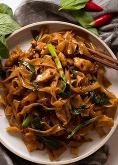 a white bowl filled with noodles and meat on top of a table next to chopsticks