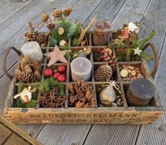 a wooden crate filled with pine cones, candles and other christmas decorations on a deck