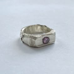 a silver ring with a pink stone in the center on a white tablecloth background