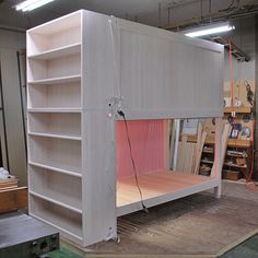 an unfinished bunk bed in the middle of a room with lots of shelves on it