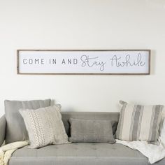 a couch with pillows and a sign above it that says come in and stay awhile