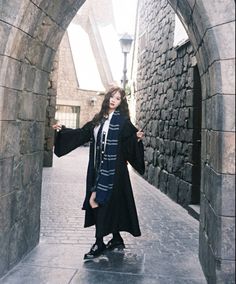 a woman is standing in an archway with her arms spread out and she is wearing a long black coat