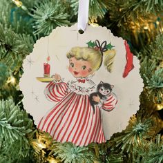 a christmas ornament with a girl holding a candle and a cat on it