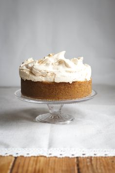 a cake with white frosting sitting on top of a glass plate next to a wooden table