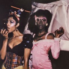 two women dressed in costumes posing for the camera with one holding her hand up to her face