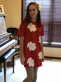 a girl standing in front of a piano wearing a red dress with white leaves on it