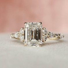 an emerald cut engagement ring with three diamonds on the band and side stones around the band