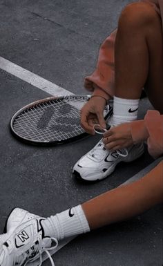 a tennis player tying his shoes on the ground with her racket and shoe laces