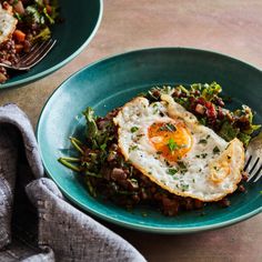 two plates with eggs, beans and greens on them next to a fork and napkin