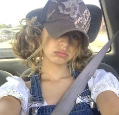 a woman wearing overalls and a hat sitting in the back seat of a car