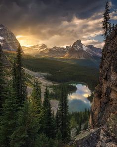 the sun is setting over a mountain lake and trees in the foreground, with mountains in the background