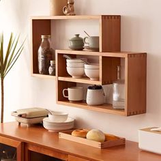 a wooden shelf filled with bowls and plates on top of a table next to a plant