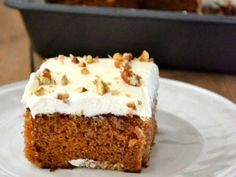 a piece of carrot cake on a plate with frosting and pecans in the background