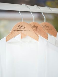 two wooden shirts hang from a white coat rack with personalized names on them,