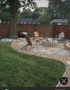 an outdoor fire pit surrounded by lawn chairs and graveled area with trees in the background