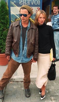 a man and woman standing next to each other in front of a flower shop on the sidewalk