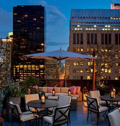 an outdoor seating area with tables and umbrellas in the city at night, overlooking skyscrapers