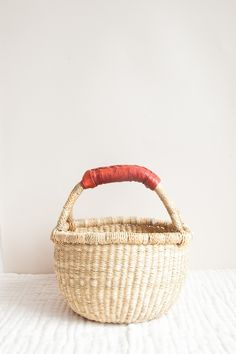 a small basket with a red handle sitting on top of a white bed next to a wall