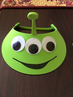 a green paper plate with googly eyes sitting on top of a wooden table next to a mouse pad