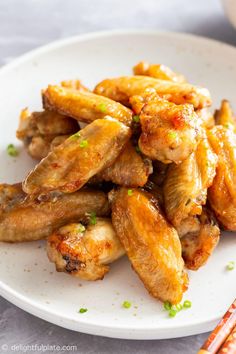 chicken wings on a white plate with chopsticks and sauce in the bowl next to it