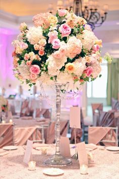 a tall vase filled with lots of pink and white flowers on top of a table