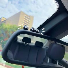 the interior of a car with three eyes on it's side mirror and buildings in the background