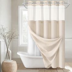 a white bath tub sitting under a window next to a shower curtain with a light colored fabric on it