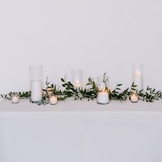 candles are lined up on a table with greenery