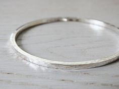 "A lovely solid sterling silver bangle, hand forged from 2.4mm square wire.  It is given a hammered texture and can be polished to a high shine or given a soft satin finish.  It can be worn on its own or as part of a set of stacking bangles. This bangle is hallmarked in the London Assay Office. The bangle is available as a circle or oval in the following sizes: SMALL   60mm  |  190mm or 7 1/2\" MEDIUM   65mm  |  204mm or 8\" LARGE   70mm  |  220m or 8 3/4\" Sizes shown are the inside diameter & circumference. Tinysilver jewellery always arrives in a lovely gift box ready to open or give away." Stacking Bangles, Hammered Bangles, Silver Rings With Stones, Mens Gold Bracelets, Wrist Wear, Silver Jewelry Design, Sparkly Things, Sterling Silver Bangle, Sterling Silver Wire Wrap