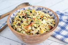 a wooden bowl filled with salad on top of a blue and white table cloth next to a spoon