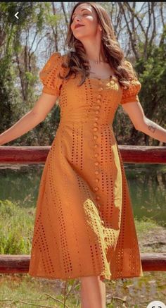 a woman in an orange dress is posing for the camera with her arms outstretched and eyes closed